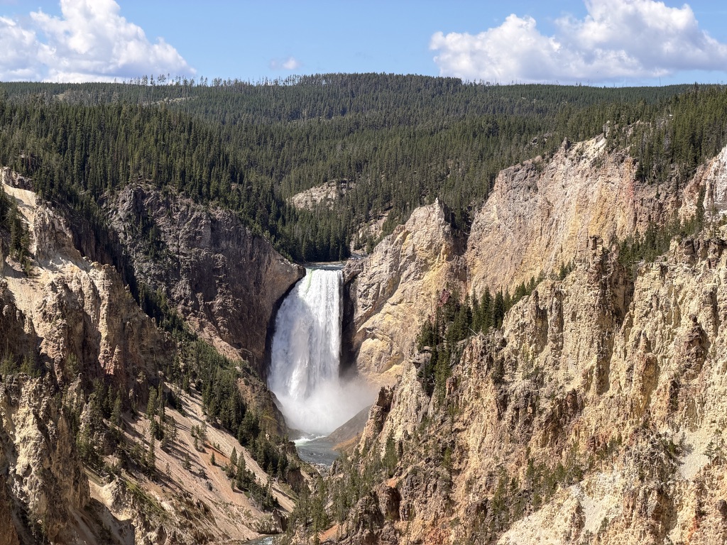 A waterfall plunges between pale canyon walls beneath a forested ridge.